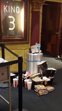 Voller Mülleimer mit Popcorn-, Nacho- und Getränkeeinwegverpackungen nach Kinovorstellung